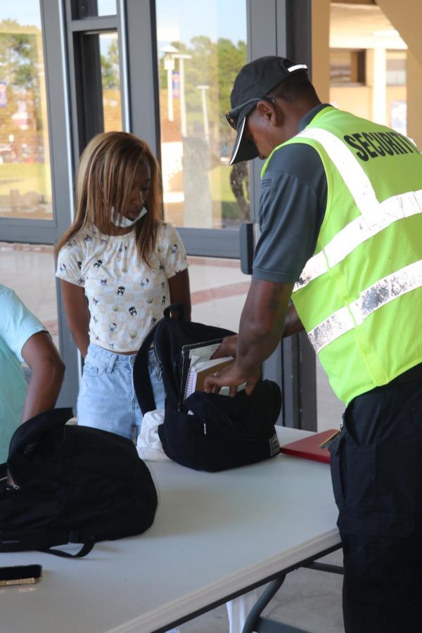 A student watches as a security officer checks through their backpack.