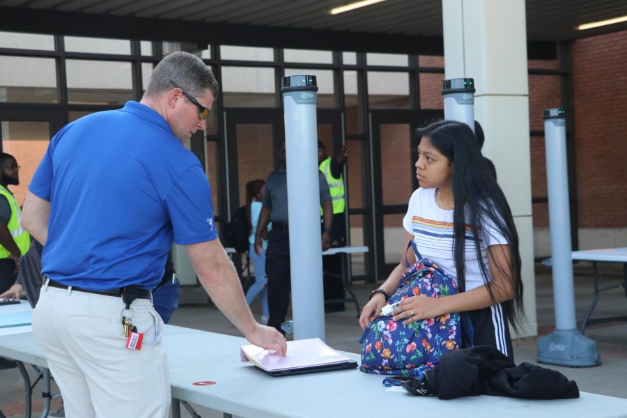 Administrator William Clark, left, helps direct a student on what items to remove from their backpack before walking through the metal detector.