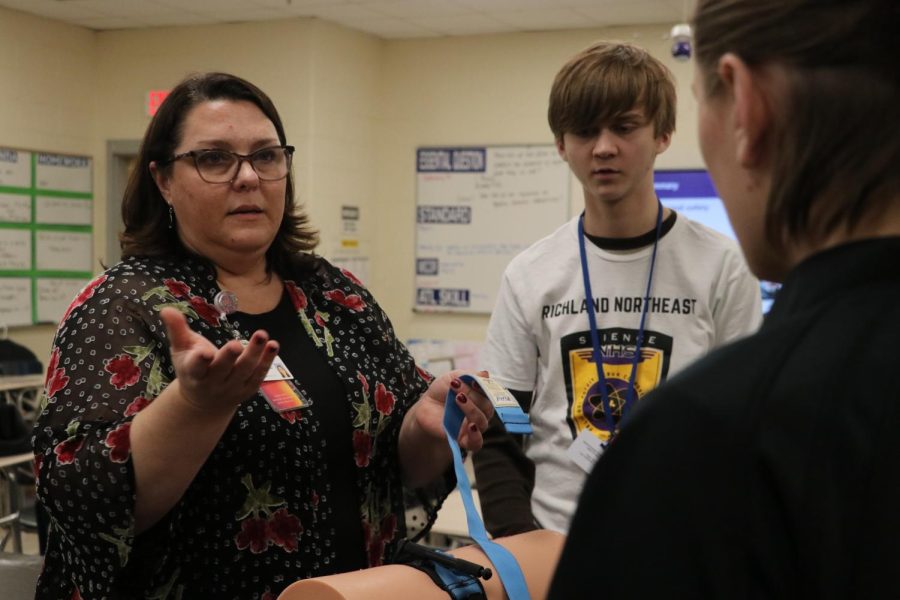 Prisma health worker, Lara Peck, explains what to do after applying a tourniquet. From left, sophomore Harris Catron and junior Kiley Wagner listen and watch on. 